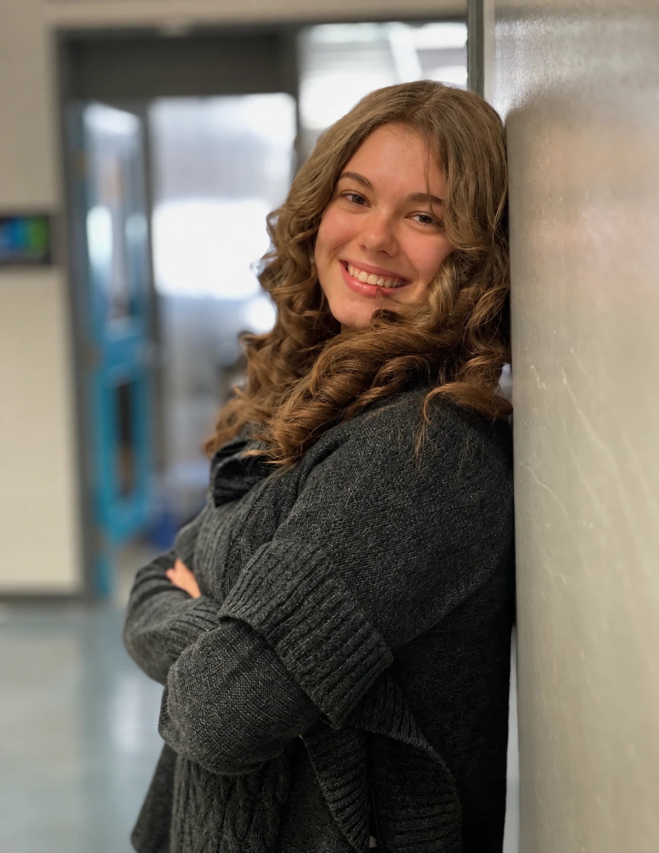 Korinna Gladhill, souriante, appuyée contre un mur, les bras croisés.